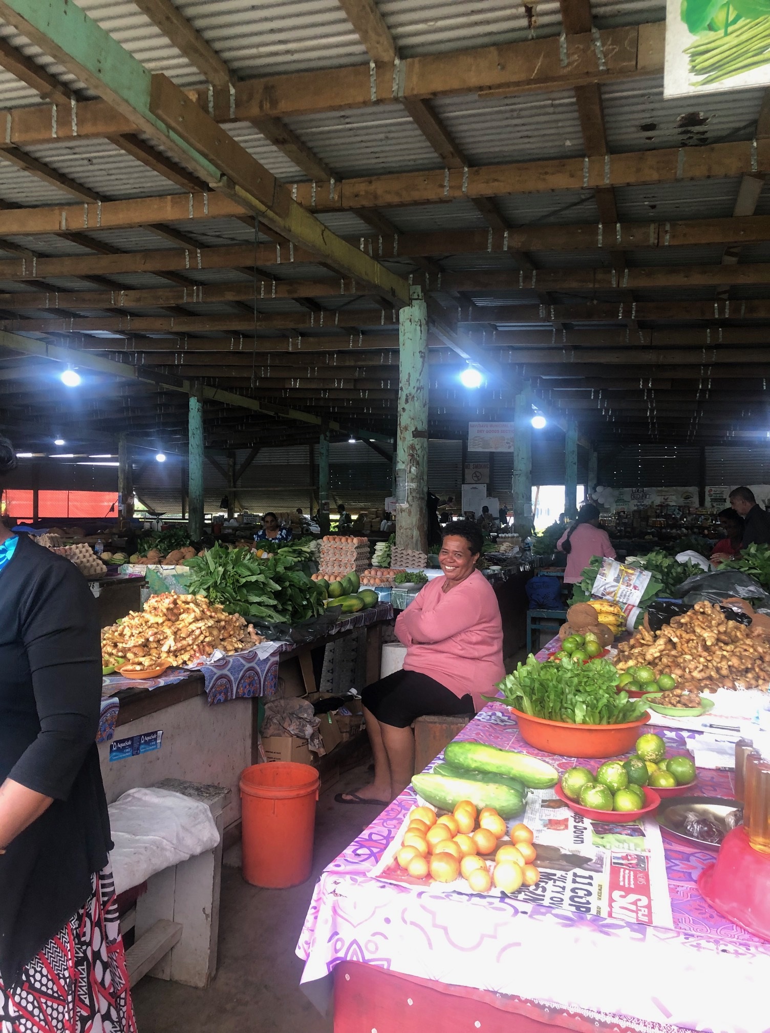 Smiling woman in front of fresh produce at the Savusavu Farmers Market in Fiji.