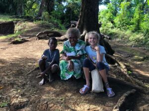 Margaret from Pentecost Island, Vanuatu, sitting outdoors with Karen and a local village boy under a large tree