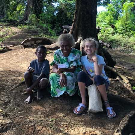 Margaret from Pentecost Island, Vanuatu, sitting outdoors with Karen and a local village boy under a large tree