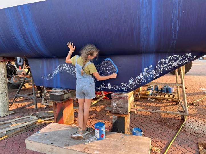 Karen peels blue painter's tape from a whale shark that she has painted on the starboard keel.