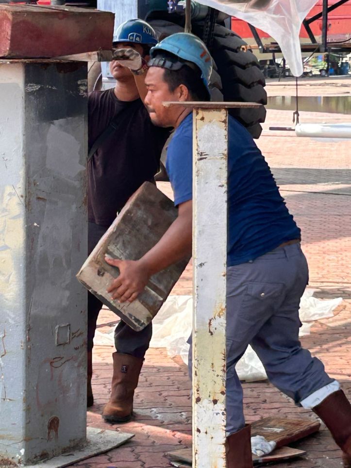 A boat worker carries heavy wood blocks at Lunas Shipyard.